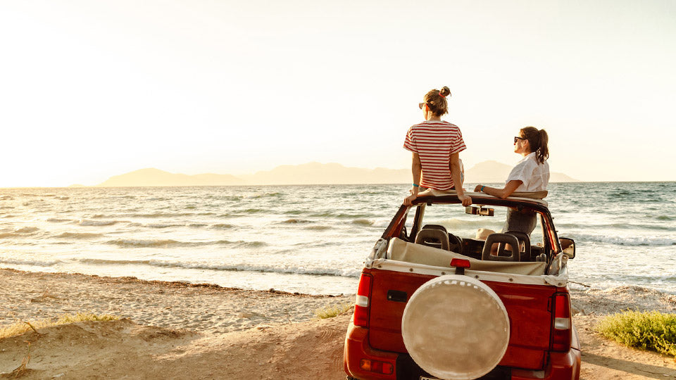 Car beside the beach with 2 people enjoying the view