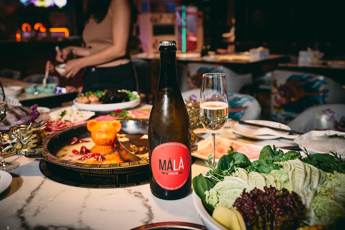 A table for Hot pot with different ingredients spread across. In the middle is a bottle of cold Mala. 