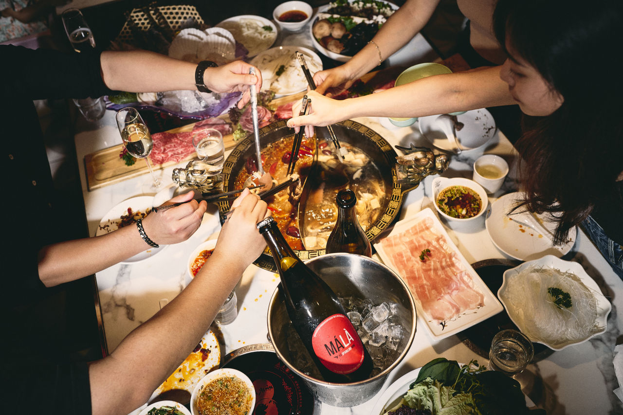 Friends enjoying a hot pot with a bottle of MÁLÀ chilled on the side.